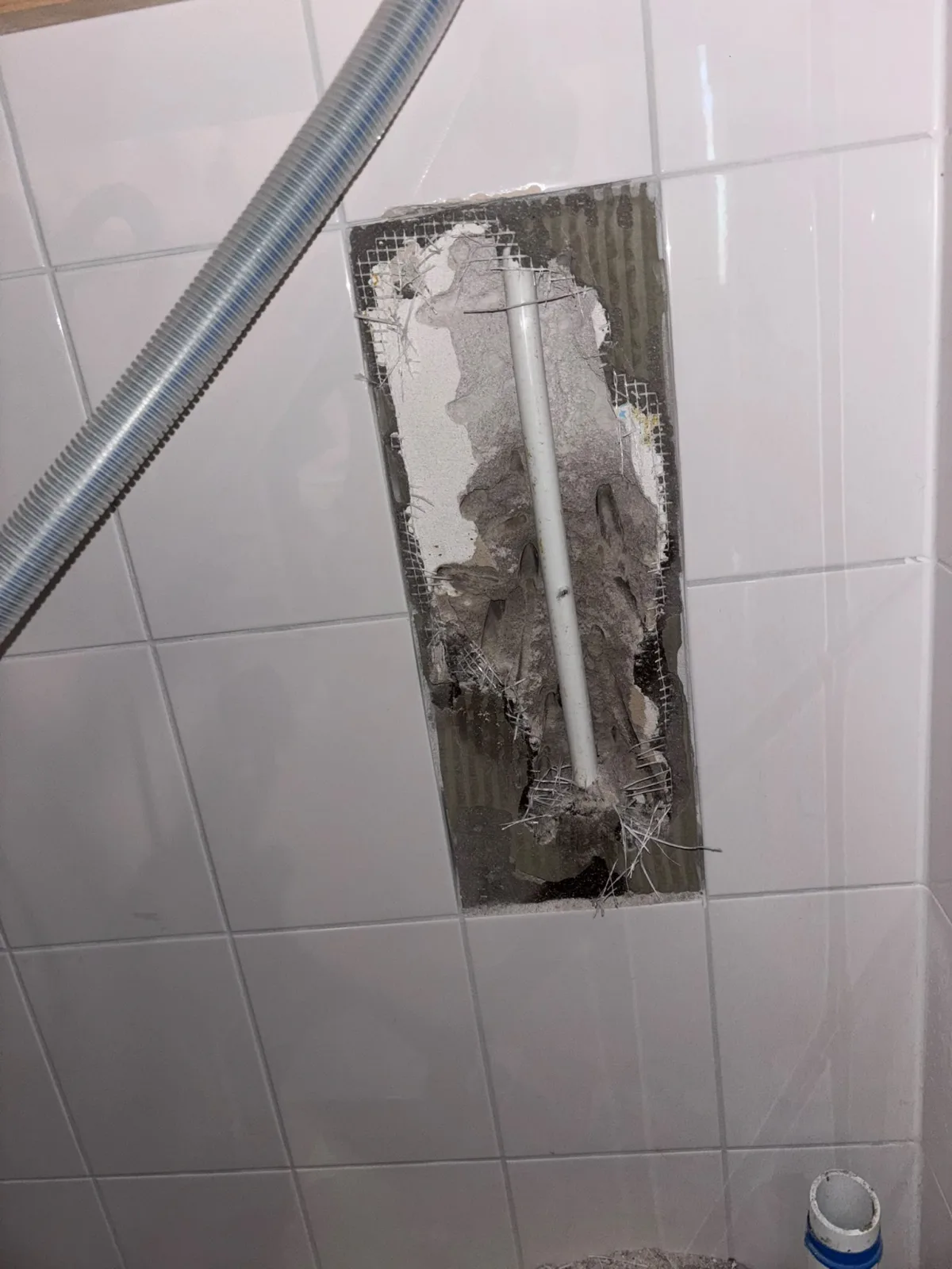 Deel tegelwand verwijderd, ingebouwde leiding en wapeningsgaas zichtbaar voor lekdetectie.