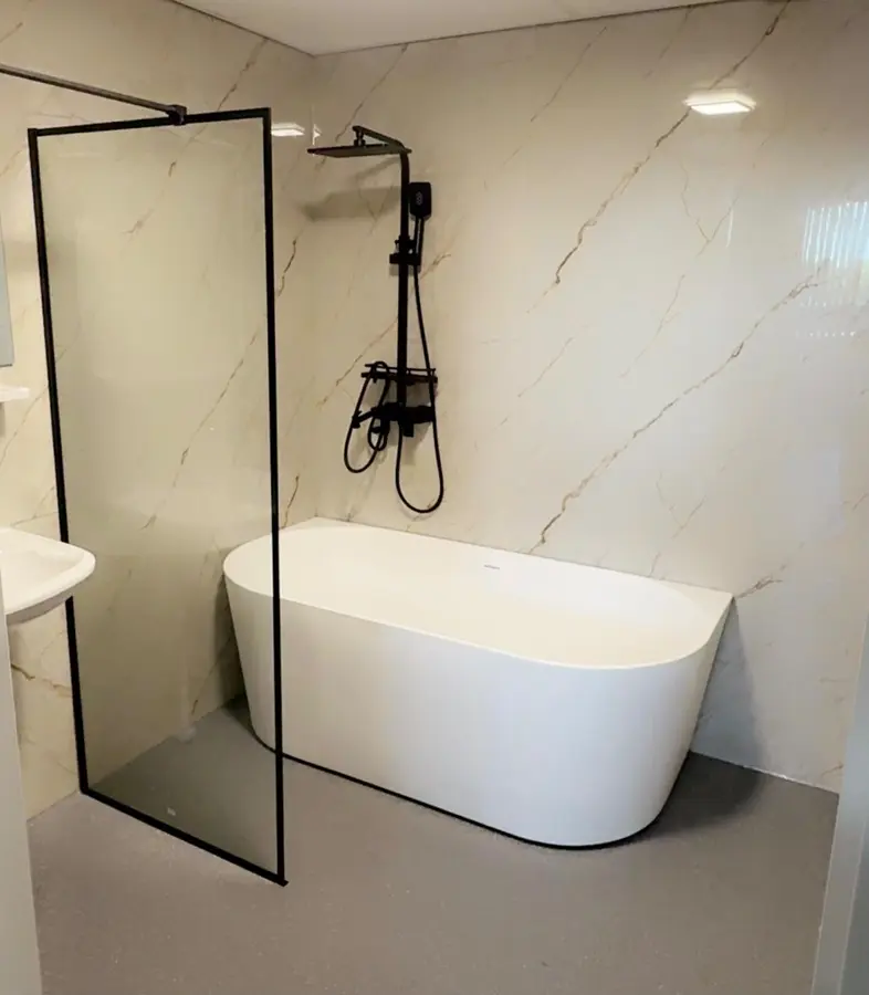 Badkamerrenovatie — Vrijstaand ligbad naast een glazen douchewand met zwart kraanwerk, wanden in marmerlook