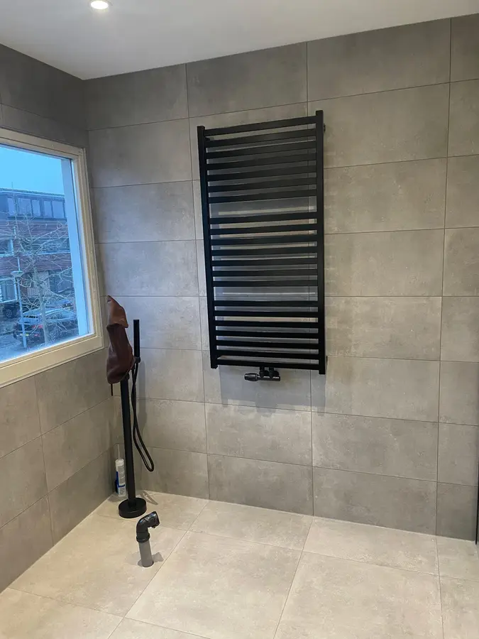 Badkamerrenovatie — Badkamer in aanbouw met zwarte handdoekradiator en aangesloten doucheslang