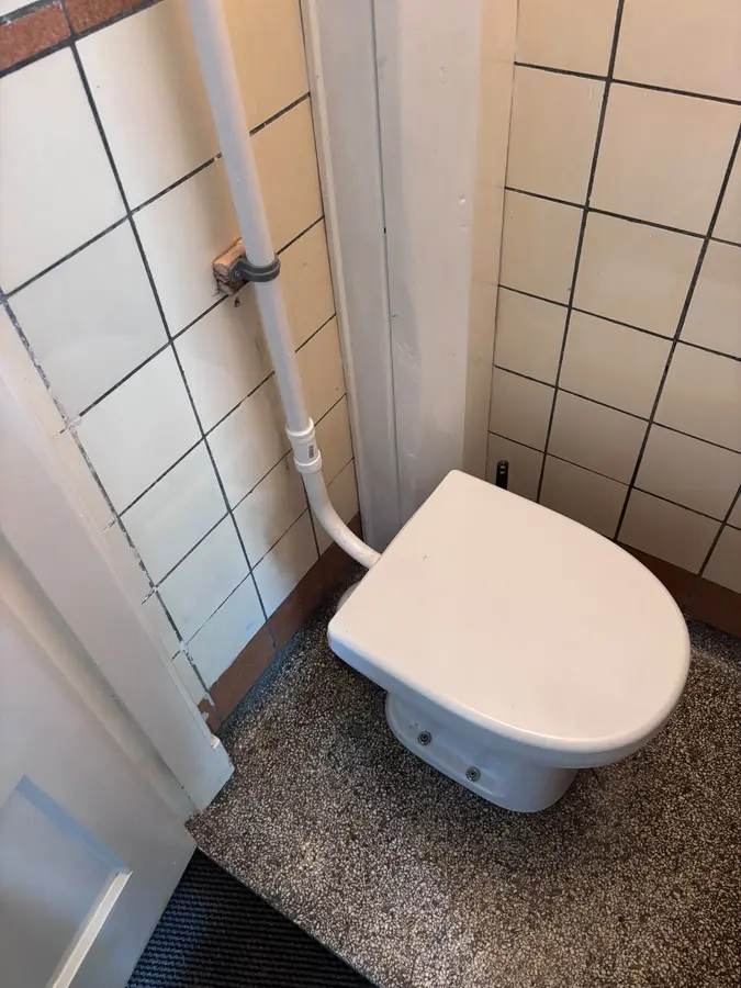 Sanitair & kranen — Toilet in een betegelde ruimte met opbouwleiding