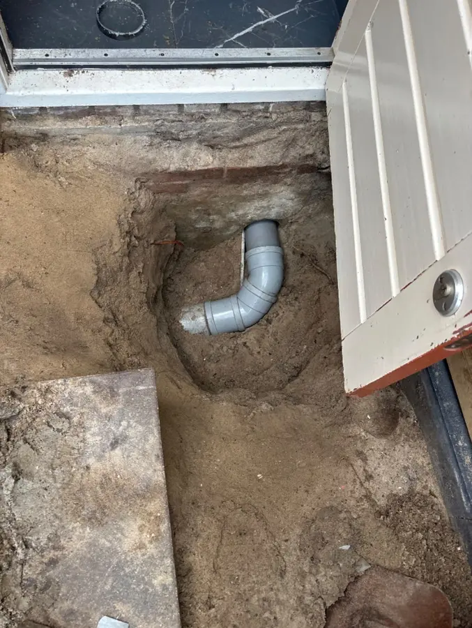 Ontstopping & riool — Opengegraven vloer met nieuwe rioolbocht naast een deurkozijn