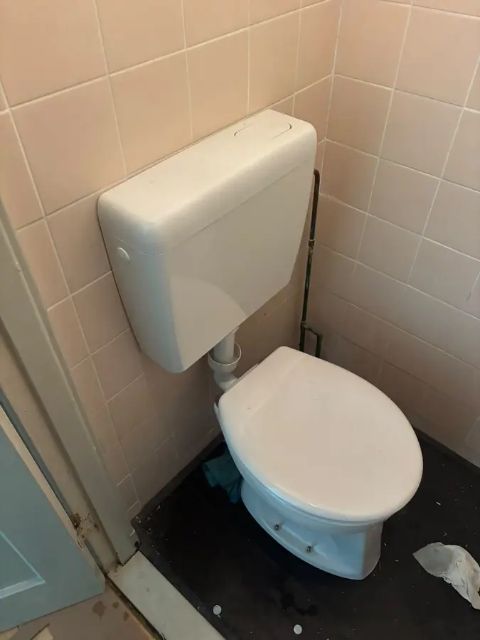 Sanitair & kranen — Toilet met opbouwstortbak in een oudere betegelde ruimte