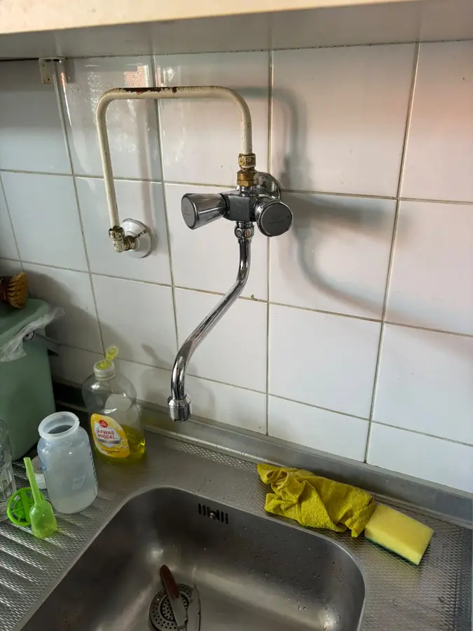 Sanitair & kranen — Keukenkraan boven een spoelbak met leiding langs de wand