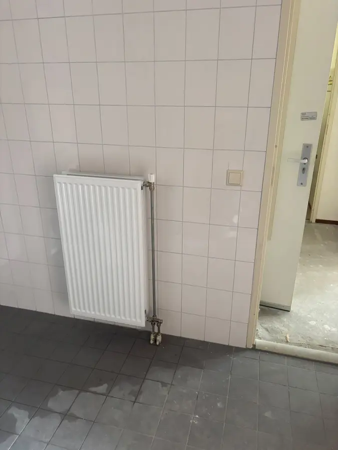 CV & verwarming — Radiator met aansluitleidingen tegen een betegelde wand