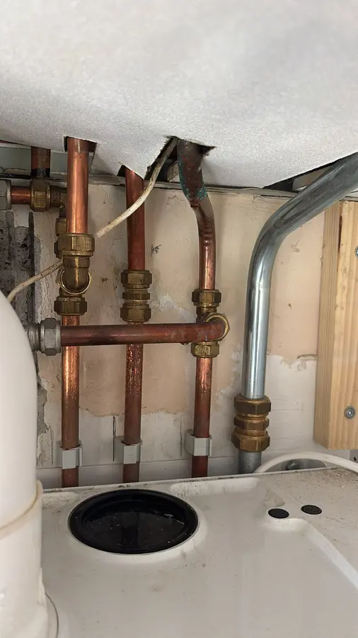 Waterleiding — Koperen leidingwerk met koppelingen boven een sanitairaansluiting